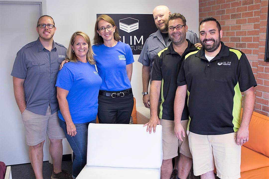 Five men and two women stand with an assembled piece of furniture.