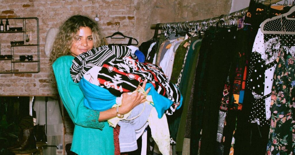 Woman in green top holding a bundle of clothes in a thrift store after reading thrift store shopping tips